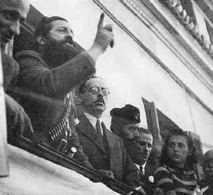 Ο μπαμπάς του Σημίτη εκ δεξιών του Άρη Βελουχιώτη την ώρα που αυτός έβγαζε το γνωστό του λόγο στη Λαμία. Από τραπεζίτης αρχικομμουνιστής! Ο Άρης αποκεφαλίστηκε, ο Γεώργιος μεγαλούργησε οικονομικά και ο υιός του διέλυσε τη χώρα