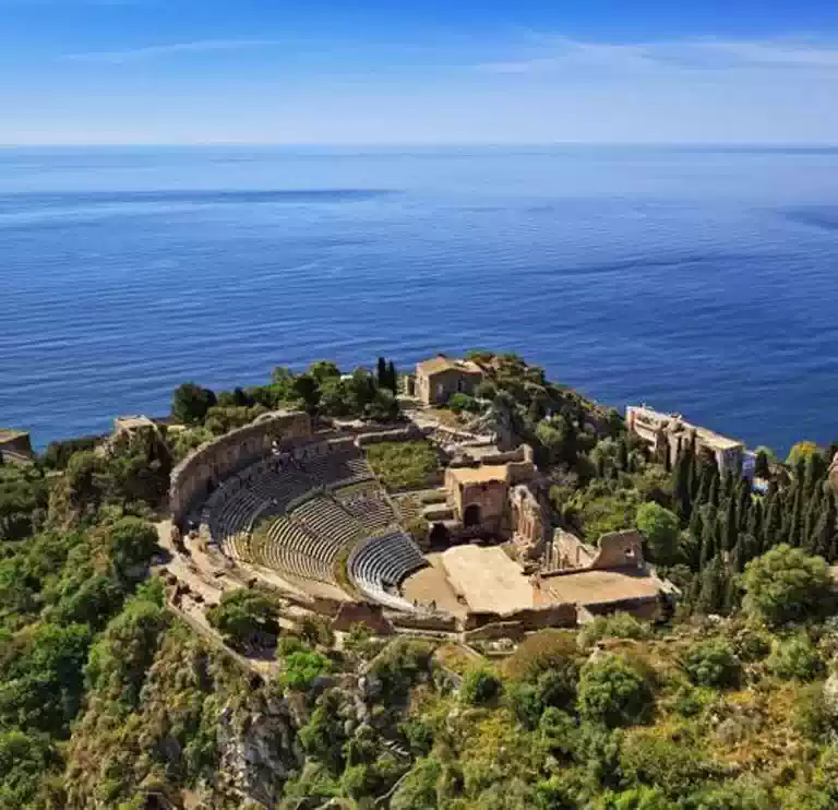 Στη φωτογραφία είναι το κόσμημα της Σικελίας, το αιώνιο «Teatro Greco» της Τaormina, το ελληνικό θέατρο στο δωρικό Ταυρομένιον. Λαξευμένο σε βράχο, διακόσια μέτρα πάνω από τον κόλπο του Giardini Naxos στο ιταλικό Ιόνιο, και κάτω από την επιβλητική όψη του ηφαιστείου της Αίτνας, στέκει εκεί πανέμορφο για να θυμίζει τη χρυσή εποχή της «Μεγάλης Ελλάδας».